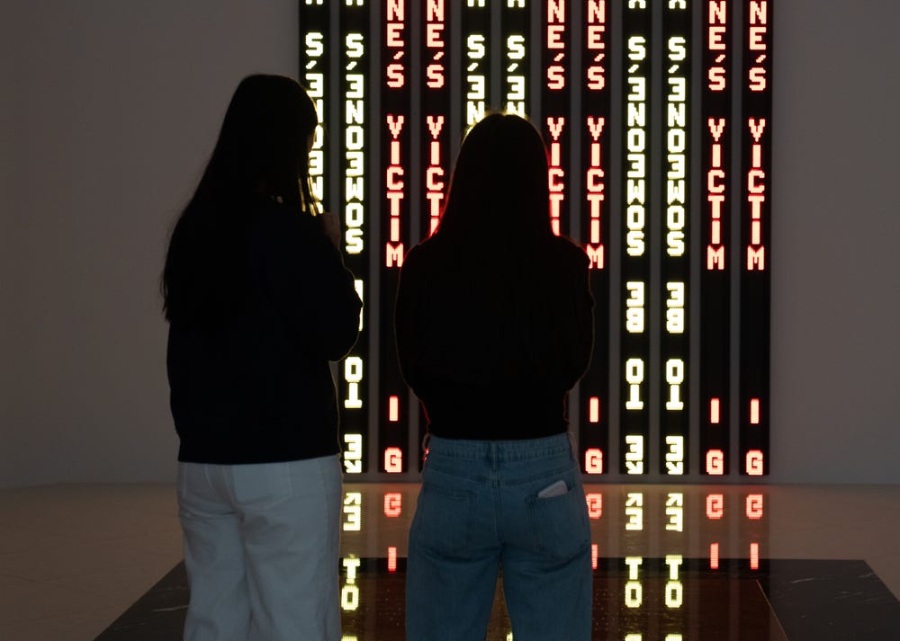 Dos visitantes frente a una obra de arte con luz LED.