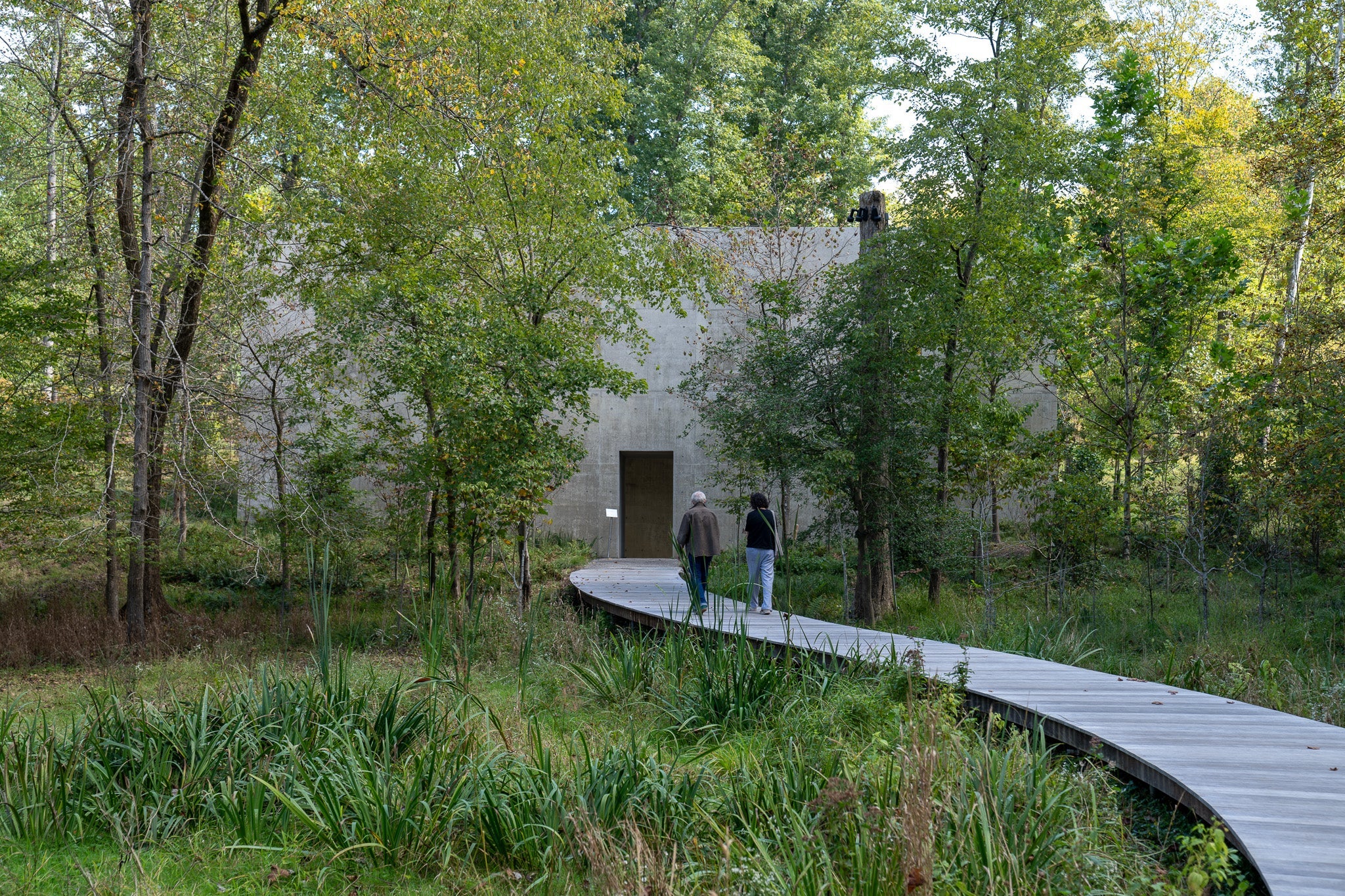Two people approach a concrete building in the wood.
