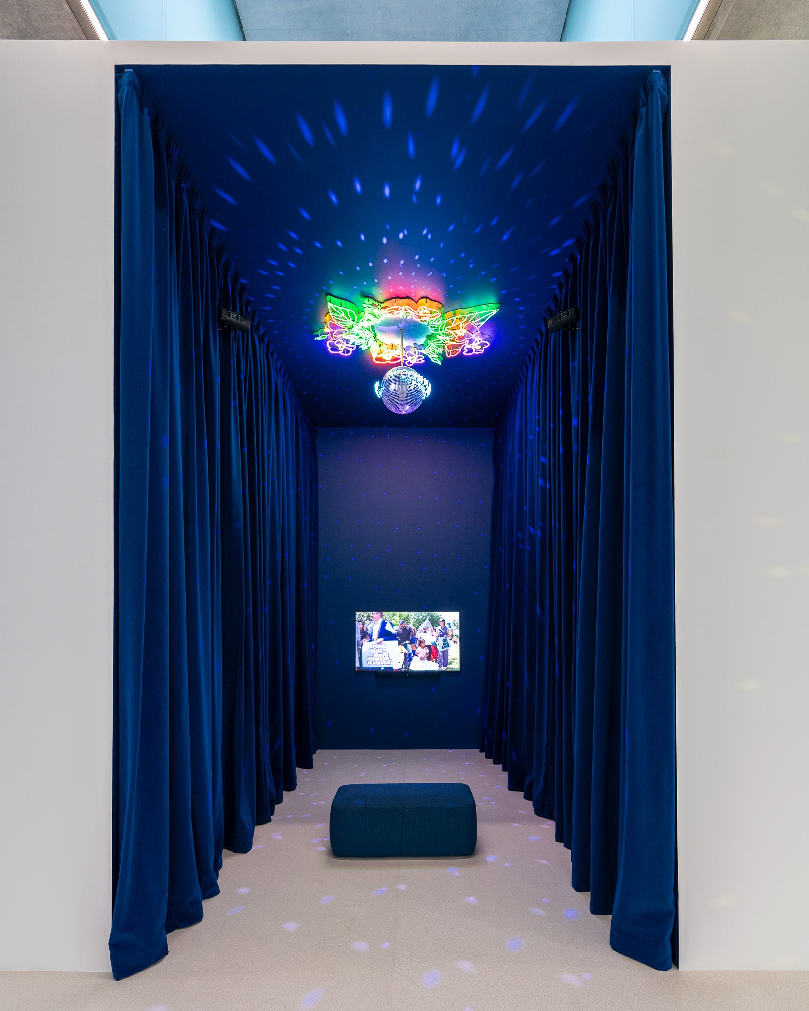 a disco ball wreathed in neon hangs in a blue, velvety room