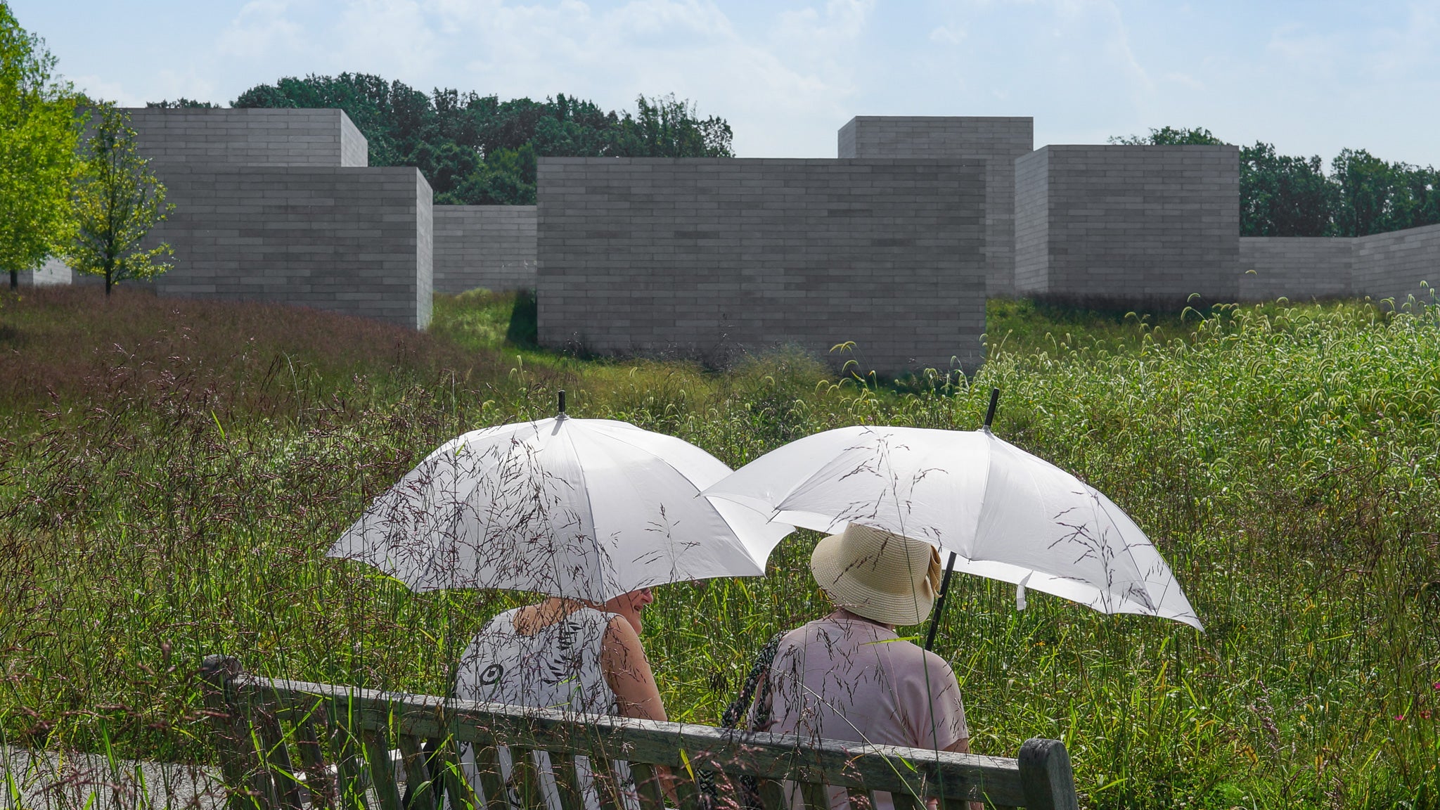 Dos mujeres están sentadas con sombrillas en un banco en el prado
