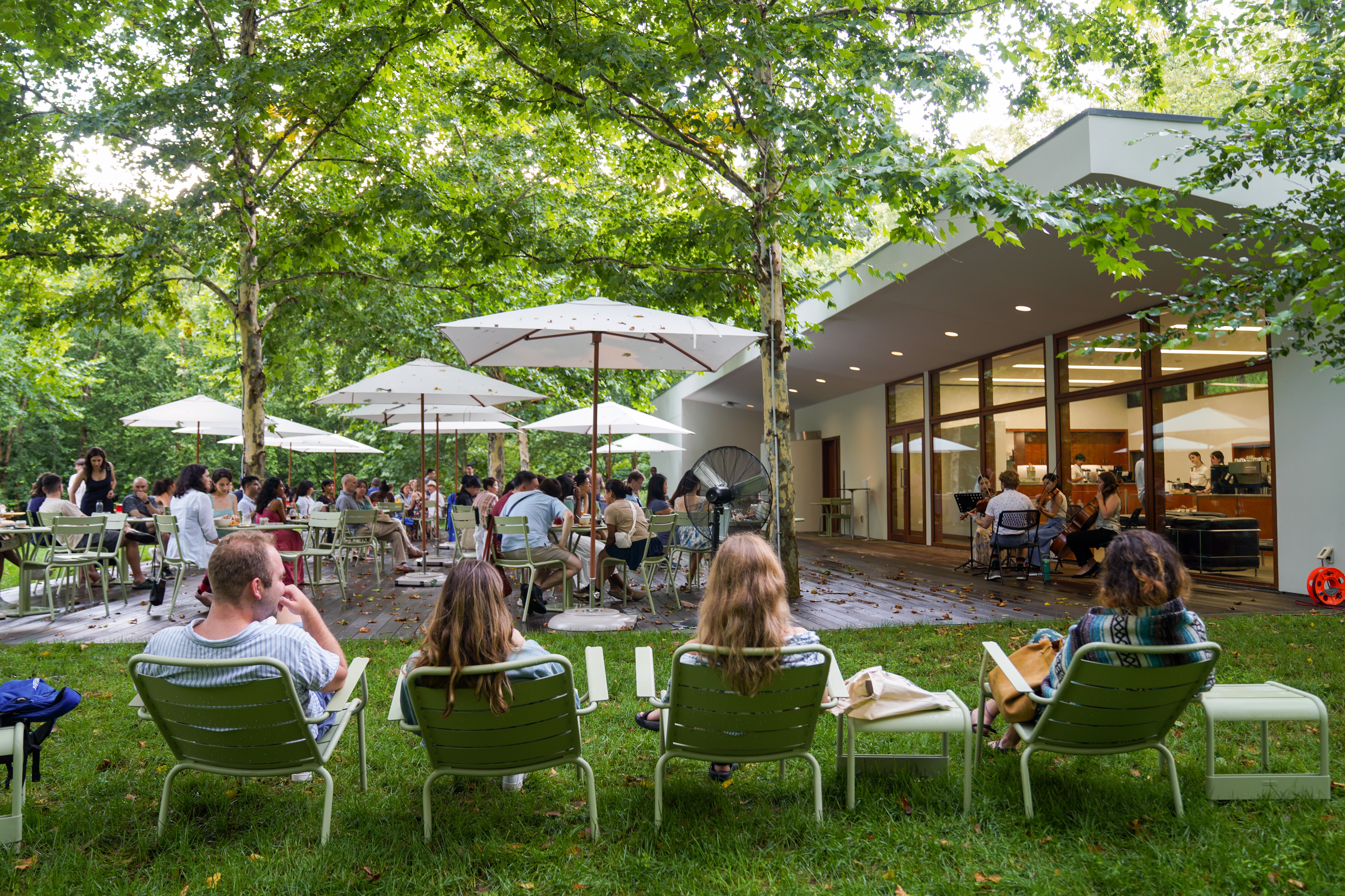 Four people sit in outdoor lounge chairs looking at a patio with a music performance