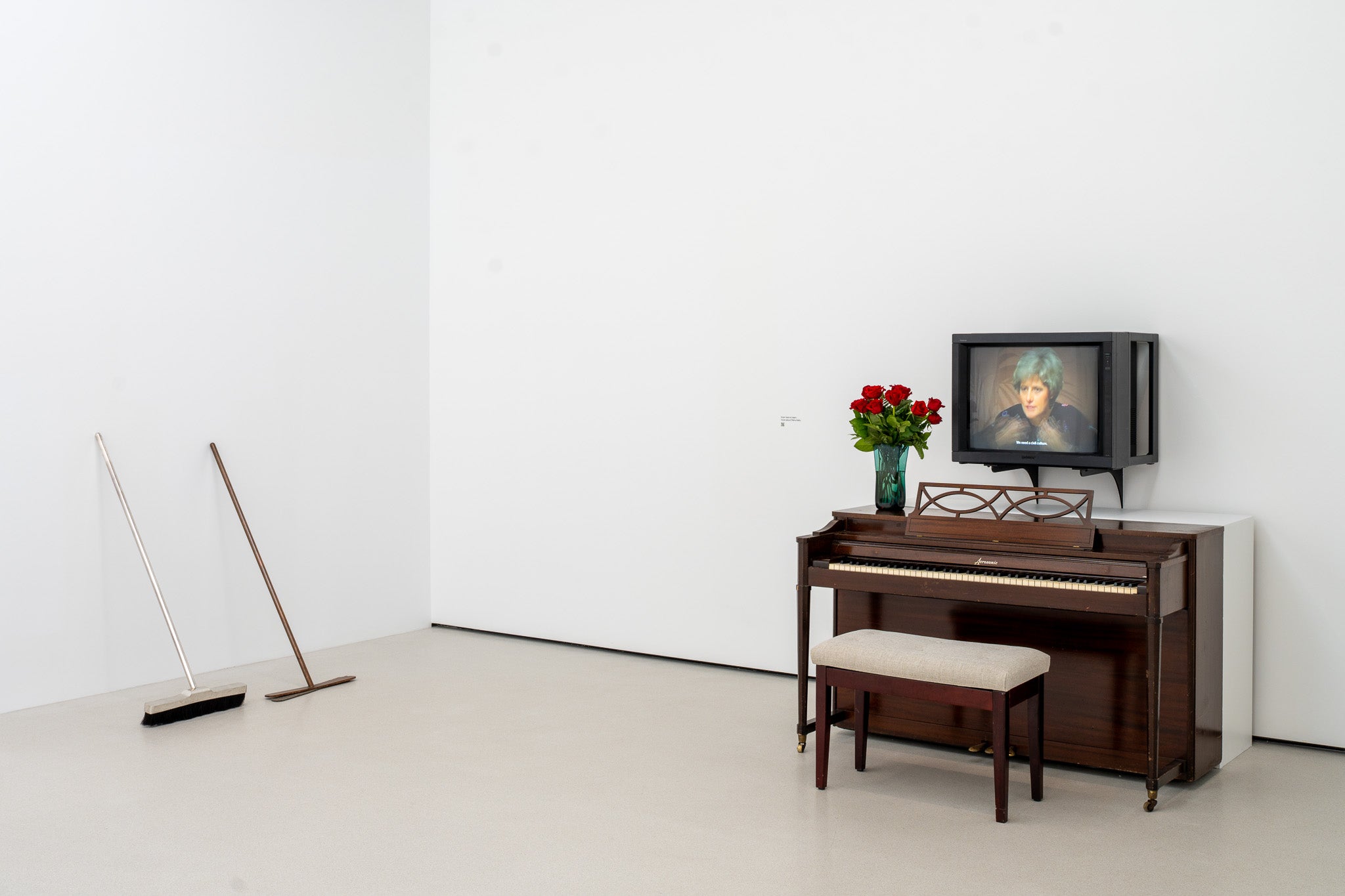 Two metal brooms rest on a wall near a piano