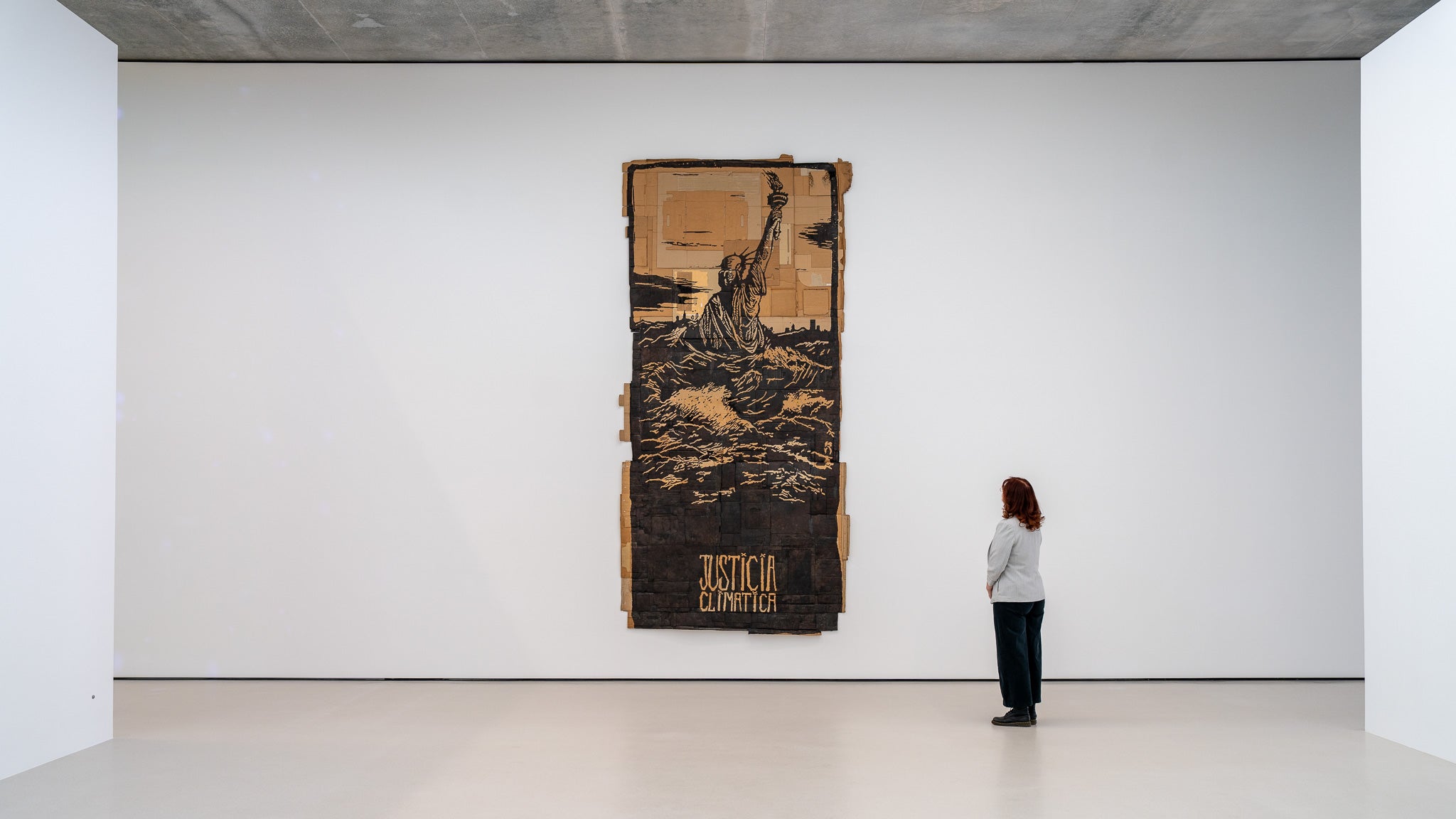 A person stands and looks at a tall cardboard work reading "justicia climatica"