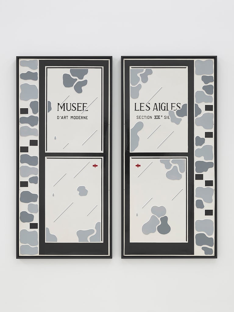 Two black-and-grey plastic panels in the shape of French doors. The left panel is labeled "Musee" above "d'art moderne" and the right says "Des Aigles" above "section XIXe sie." Parts of the text are obscured by lines and shapes.