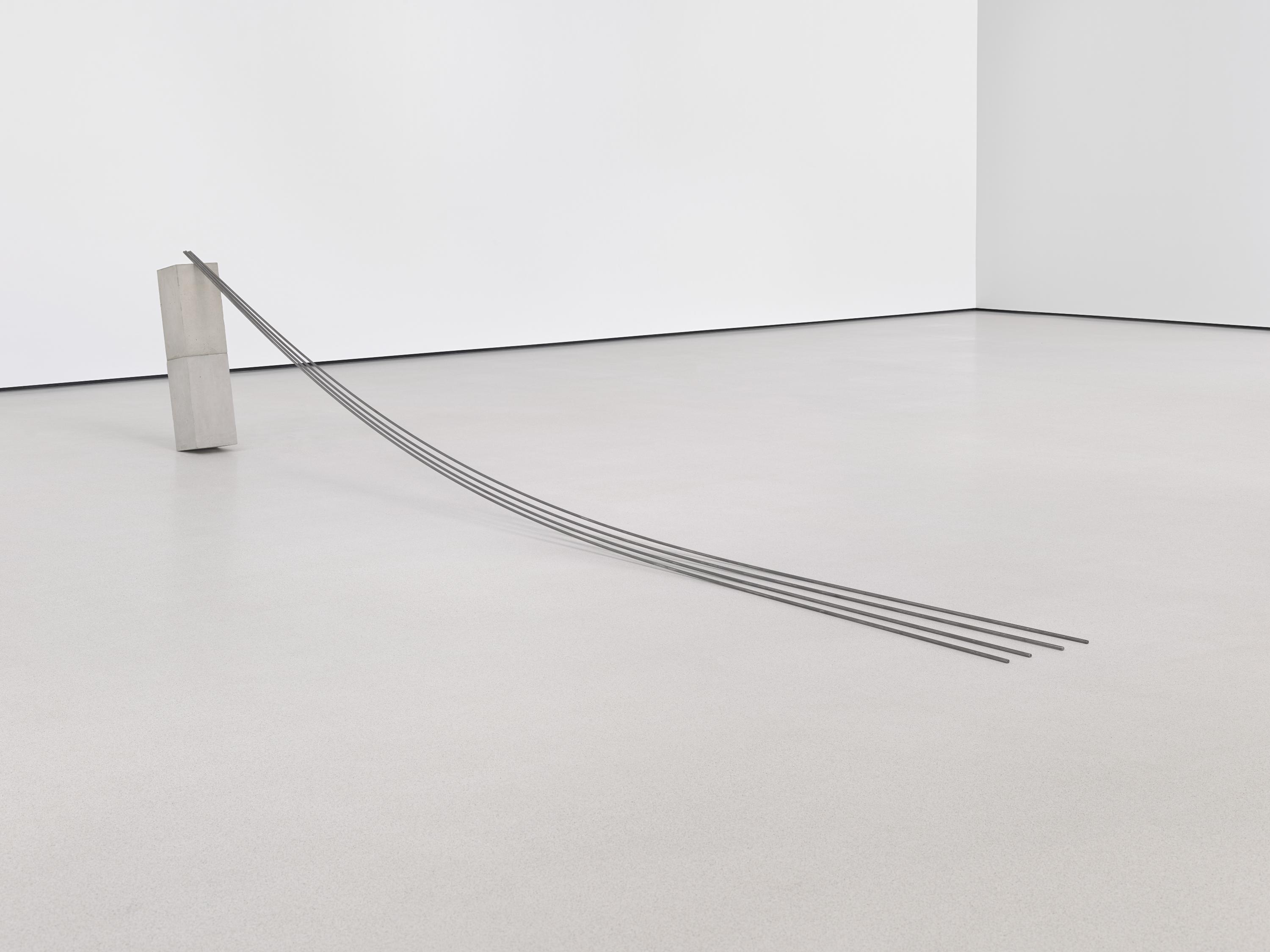 Two concrete blocks stacked vertically lean to the left, supported by four metal rods that drape to the right in an arc.