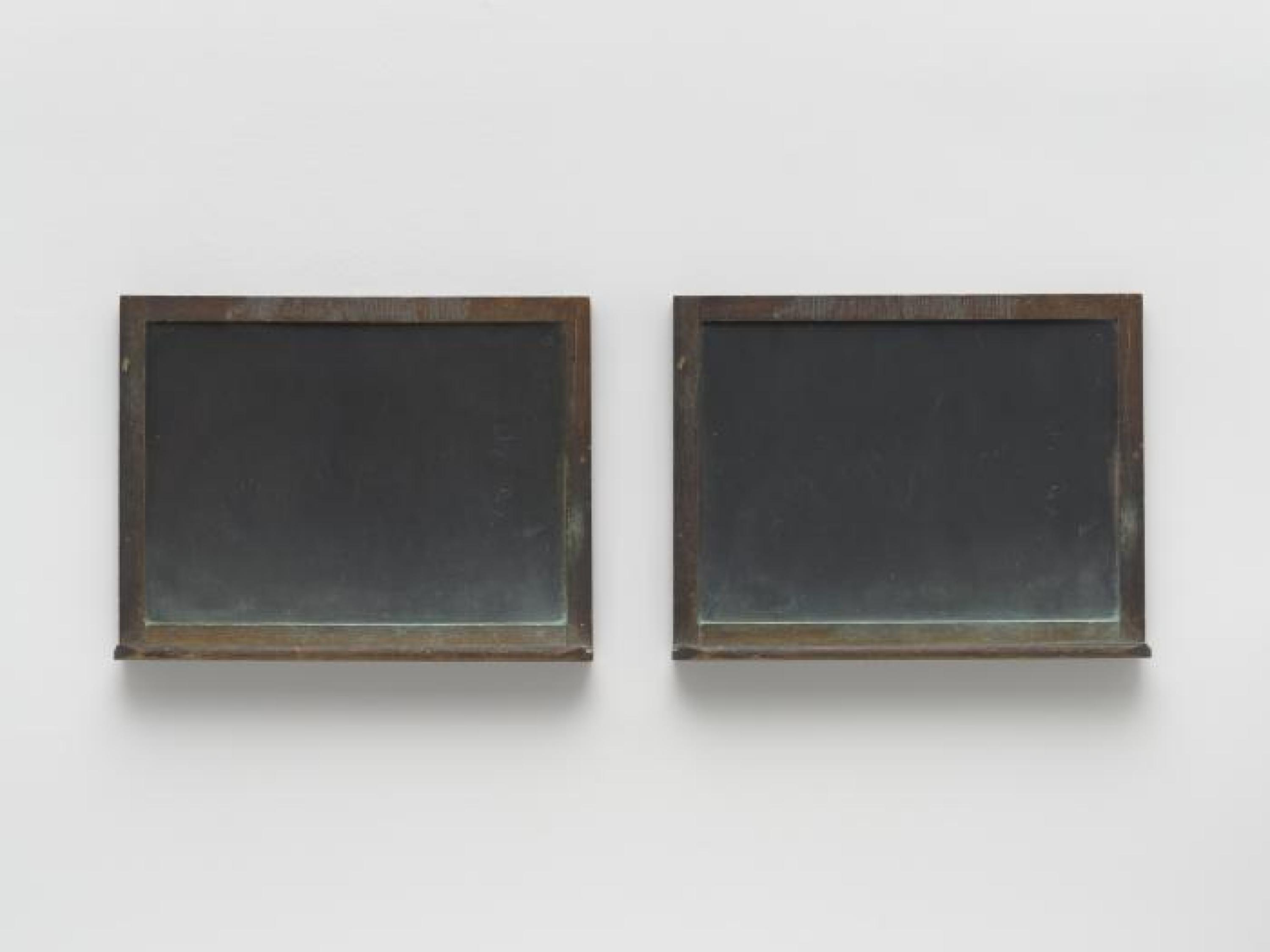 Dos pizarras enmarcadas de aspecto desgastado, ligeramente espolvoreadas con pastel teñido de verde, montadas sobre una pared blanca.