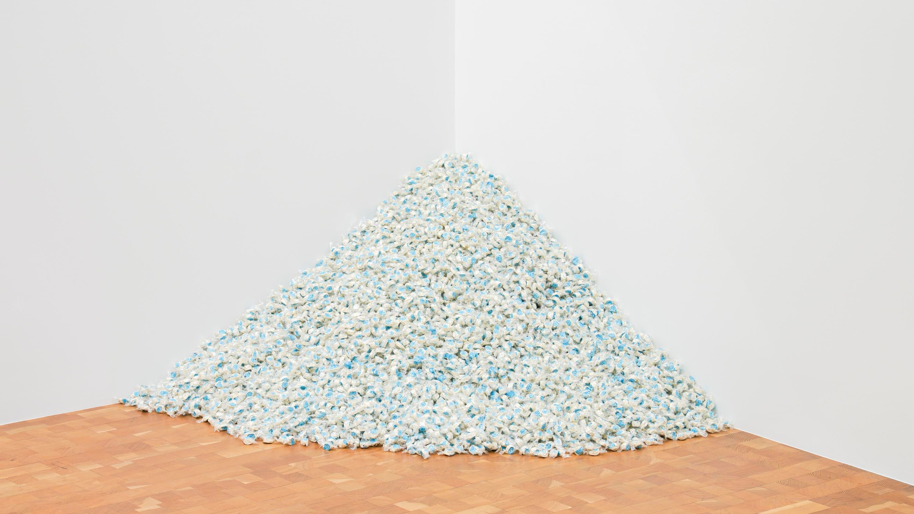 A pile of blue and white candies individually wrapped in clear plastic sits on the floor in the corner of a room.