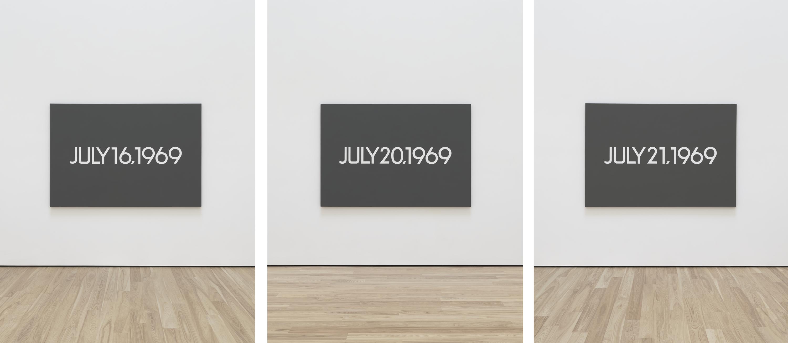 Tres lienzos de color gris oscuro, cada uno con una fecha diferente, pintada en blanco, cuelgan de una pared blanca sobre un suelo de madera clara.