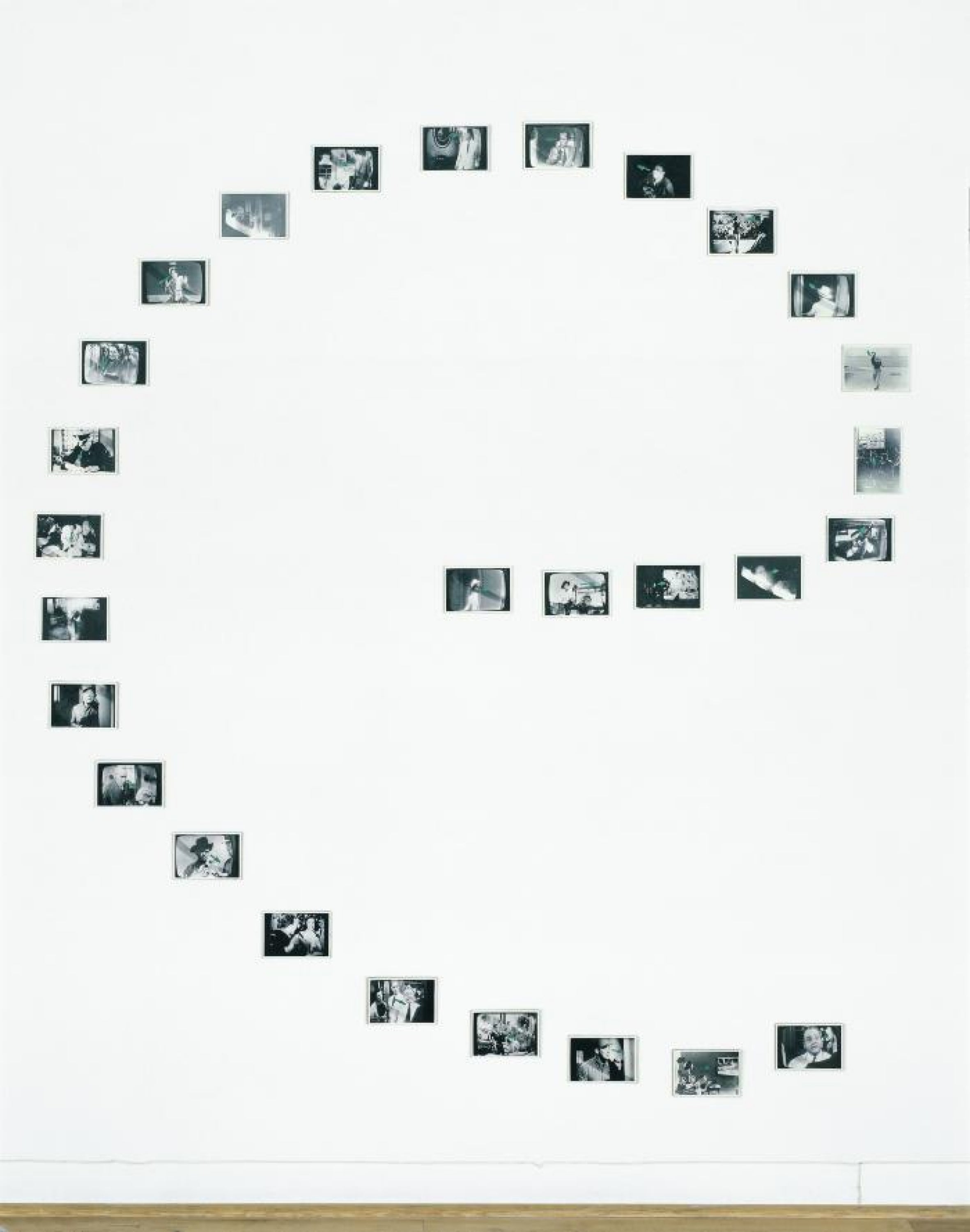 Twenty-eight black-and-white television still photographs arranged in the shape of a lowercase "e." Each photograph depicts a person looking at something, which the direction of their gaze traced in pale blue arrows. These arrows direct the form of the spiral of images.