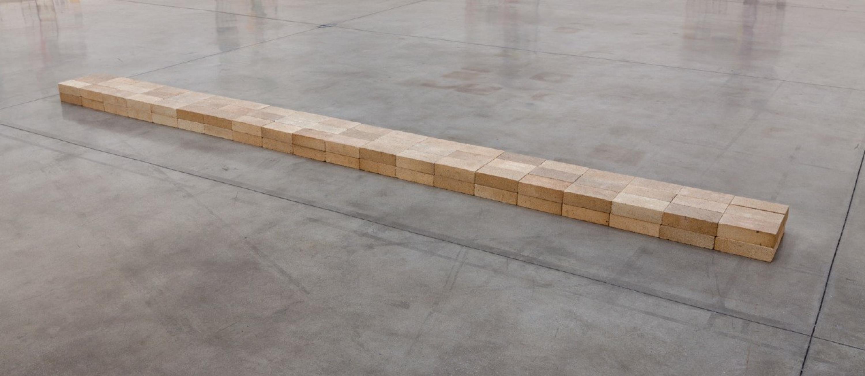Two layers of flat wood blocks arranged in a strip on a gray concrete floor.