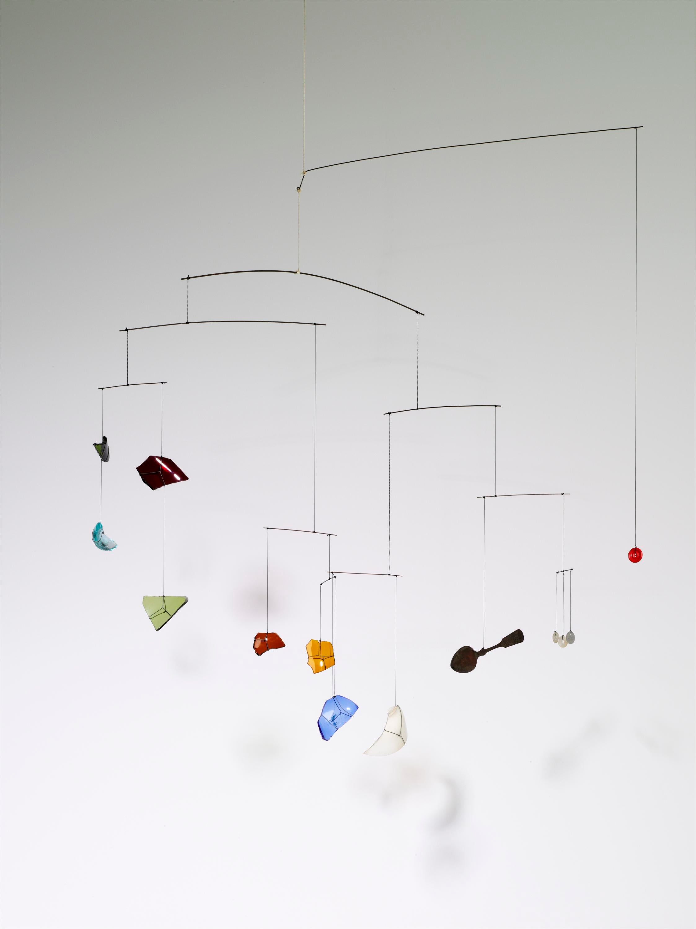 Hanging from above, this mobile boasts 10 horizontal wires balancing 23 vertical wires ending in 12 shards of glass (in multiple colors) and a black spoon.