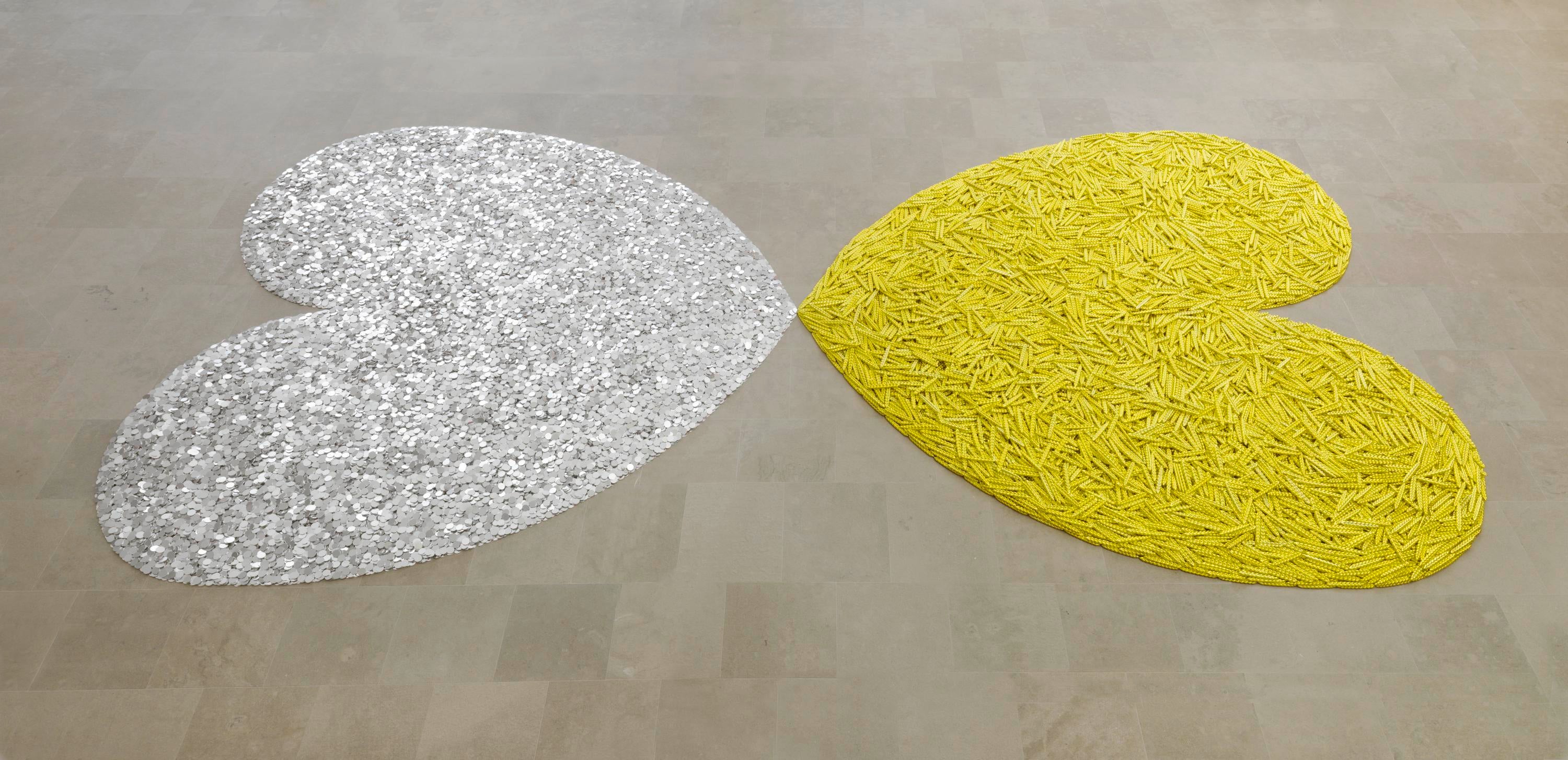 Two hearts are shaped on the floor. One is made of metallic sheafs of wheat and the other is made of coins. They touch at the tips.
