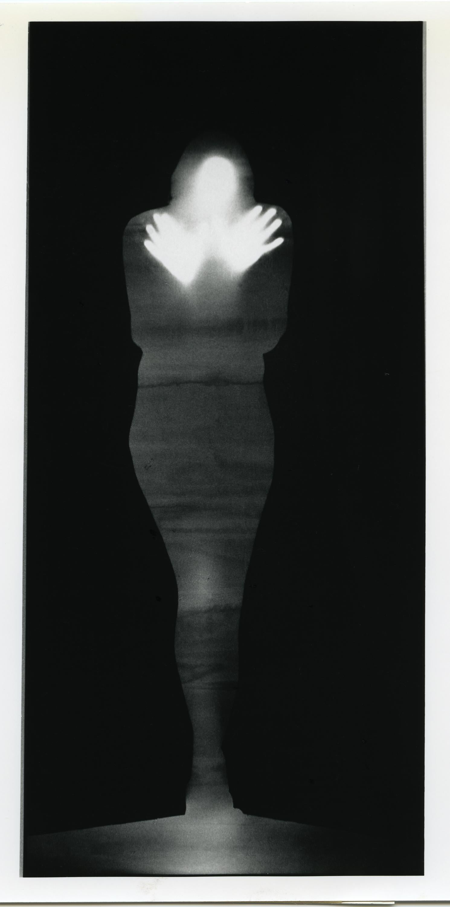 Una fotografía en blanco y negro de la silueta de una persona. La figura parece estar presionando sus manos contra la pantalla como si estuvieran detrás del lienzo.