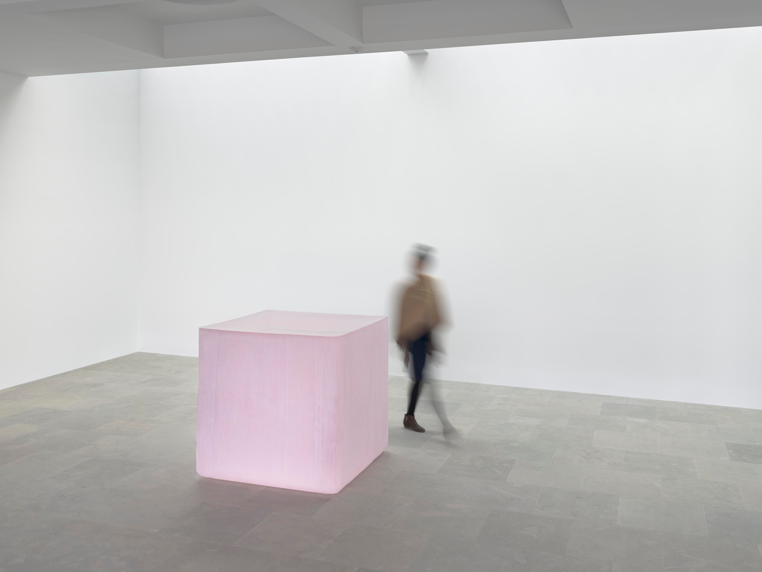 Person moving behind large pink cube.