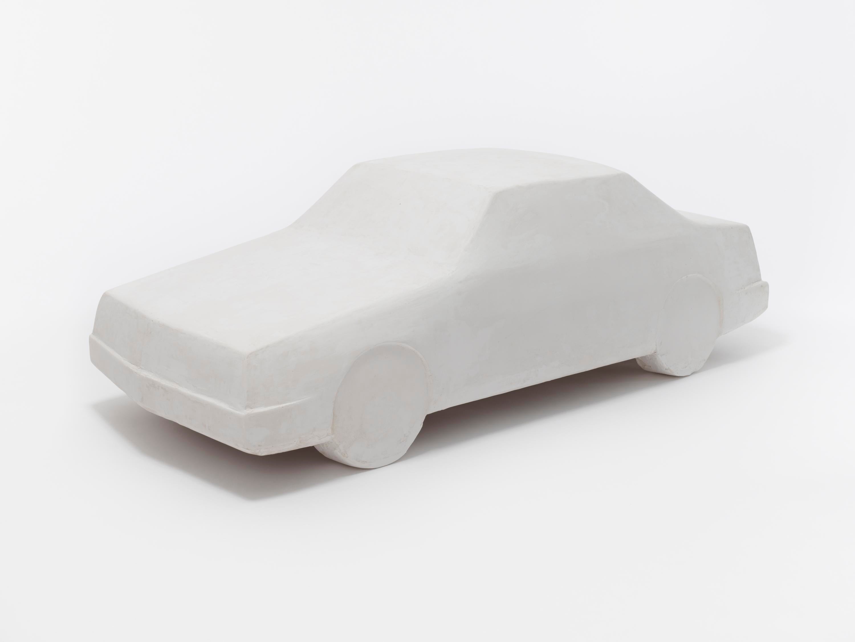 A close-up of a smooth white plaster car, with the basic shapes of a 1980s four-door sedan and no details.