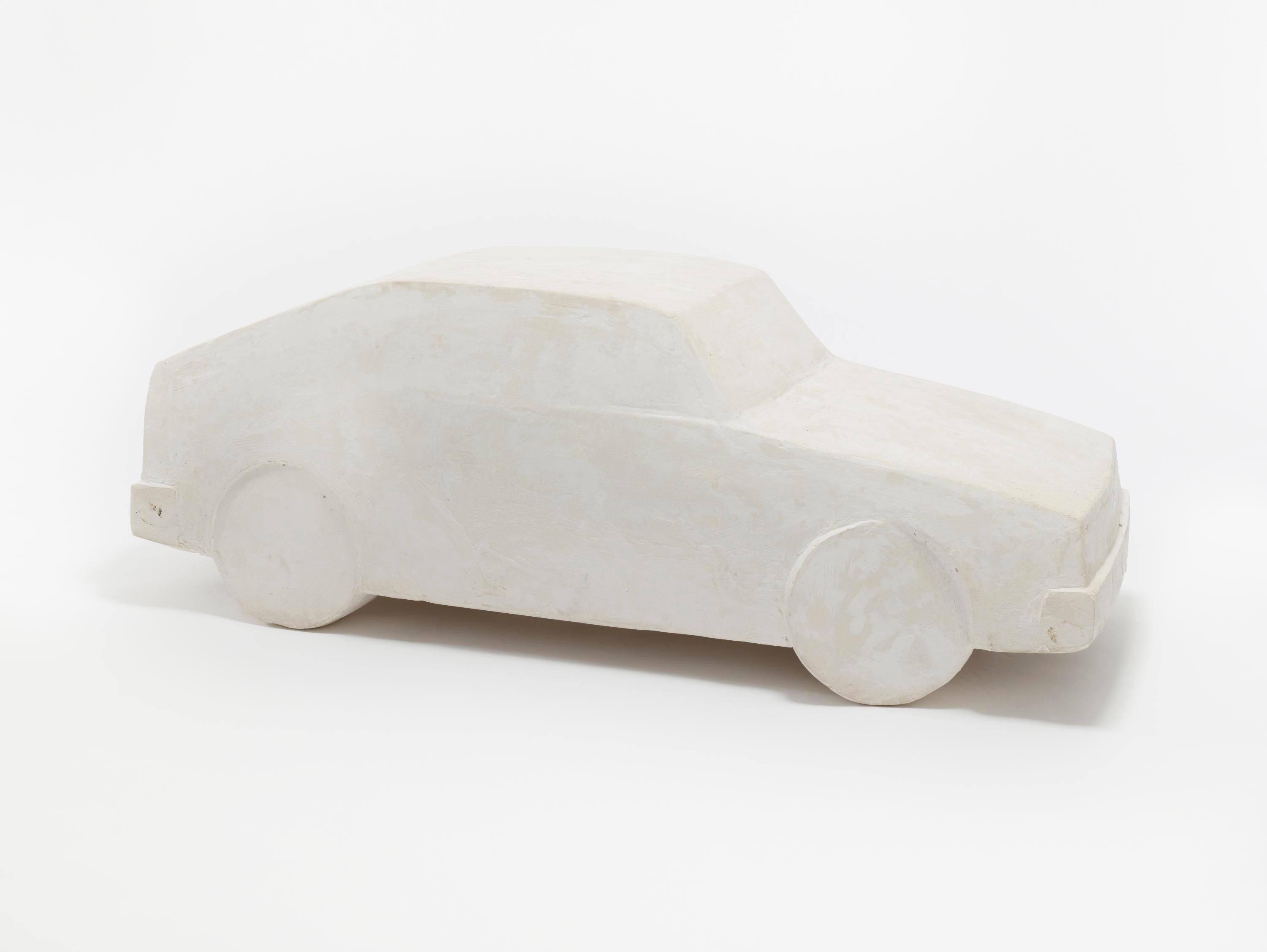 A close-up of a smooth white plaster car, with the basic shape of a 1980s hatchback. The texture of the plaster is visible.