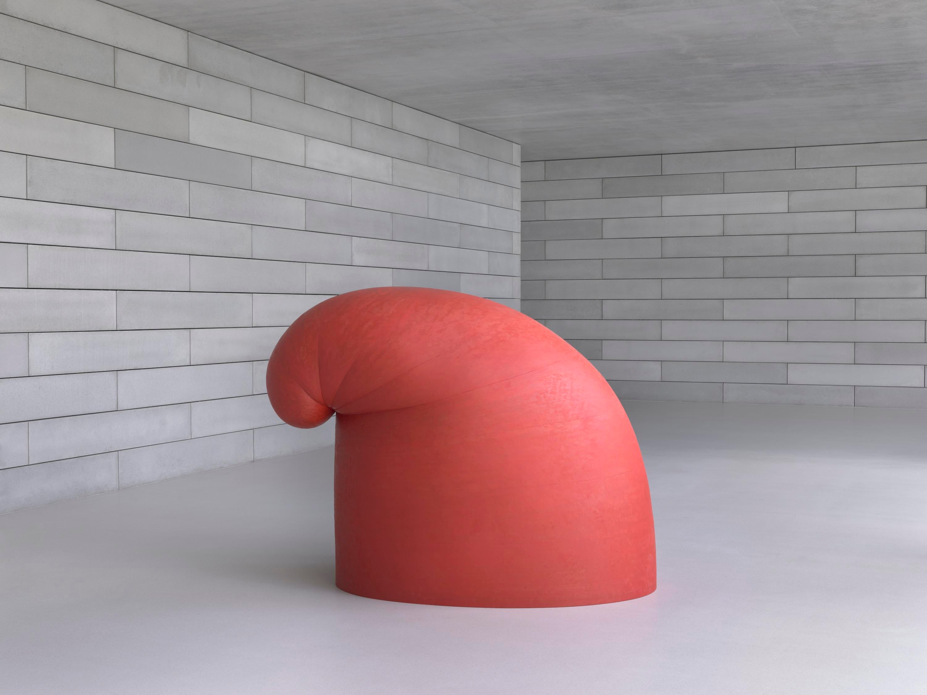 A large, rounded, red sculpture sits in a concrete room.
