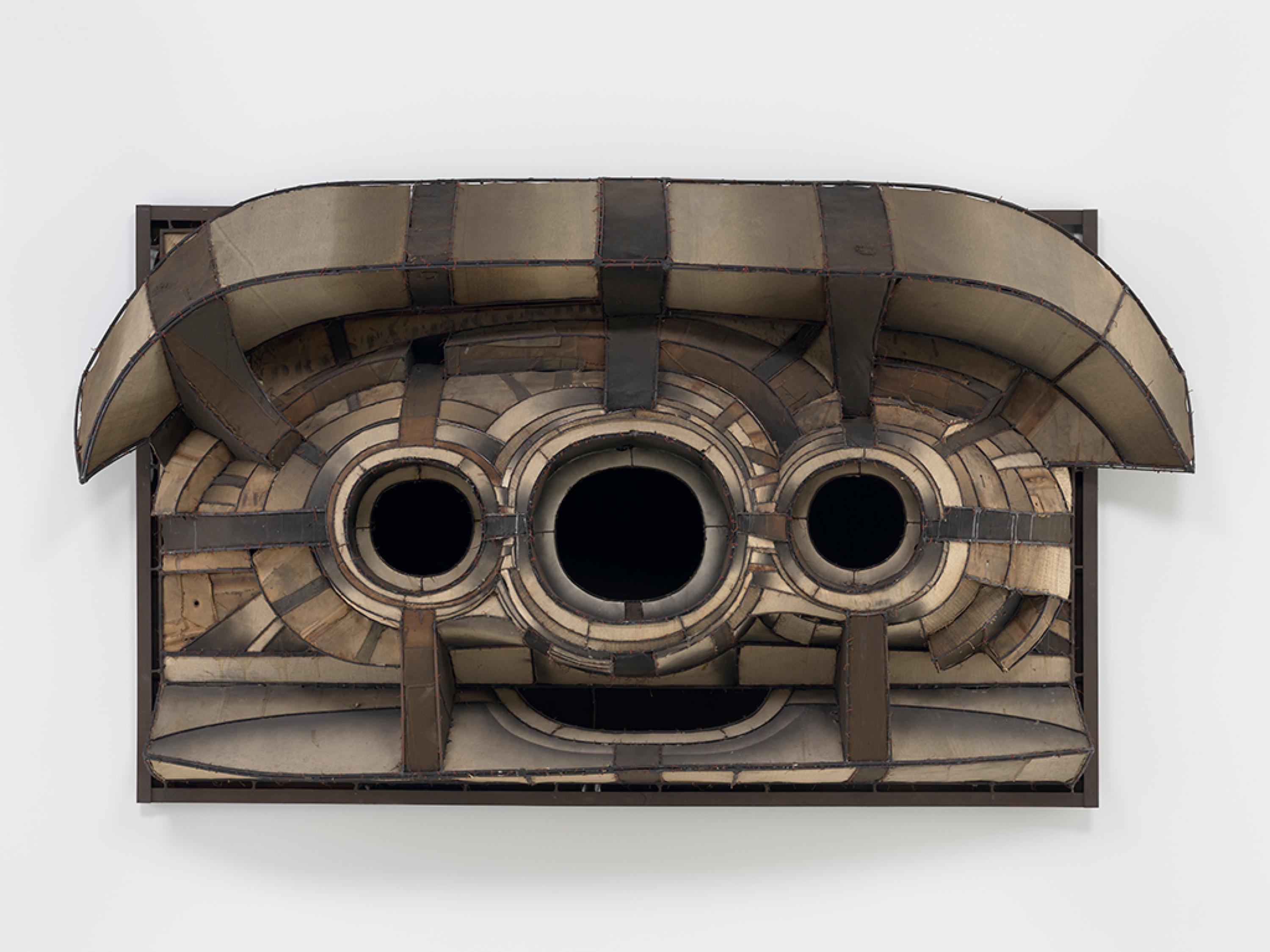 An abstracted form made from canvas, welded metal, and wire sits in relief off a white wall - three deeply black voids dominate the composition.