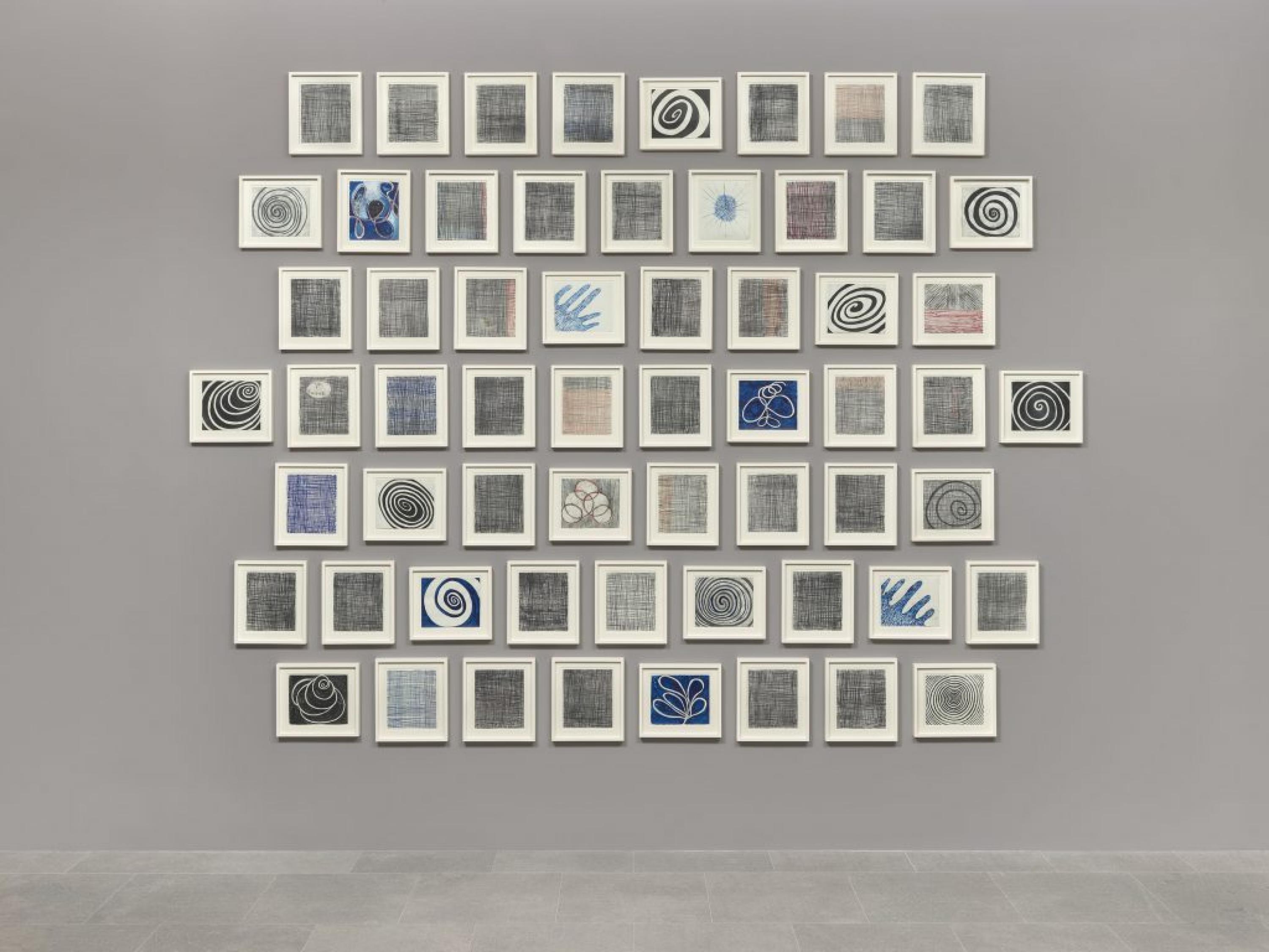 Varios dibujos formados por patrones en espiral, cuadricula y abstractos enmarcados en blanco sobre una pared gris