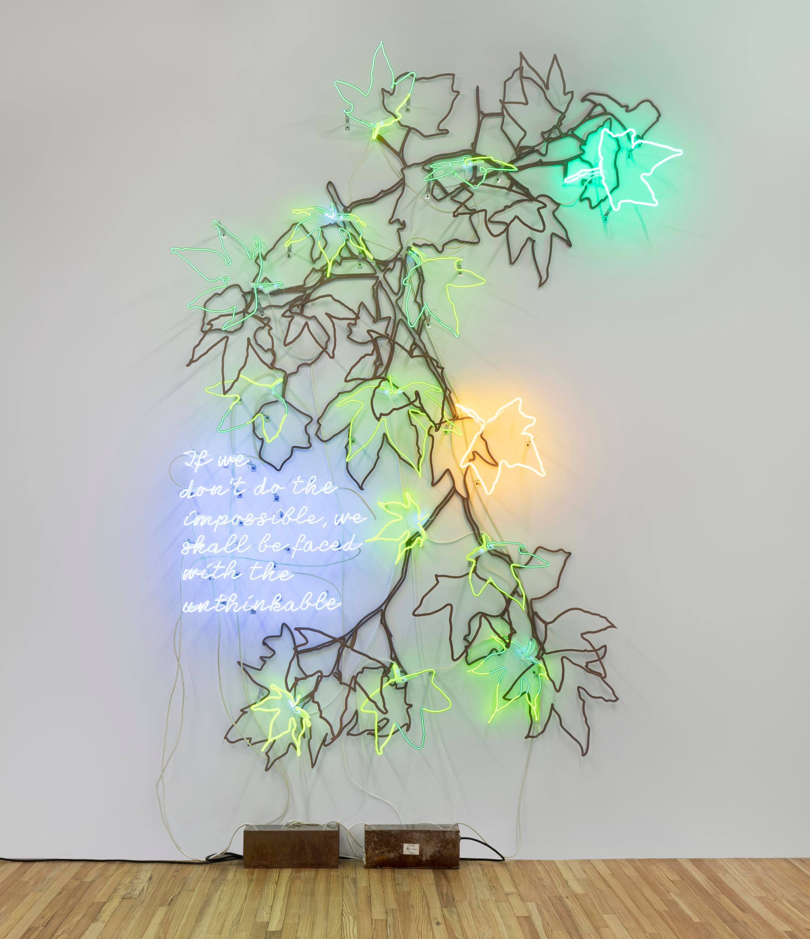 Neon tree branches and text hang on a gallery wall. The text reads Ecofeminist Sycamore Branches: If We Don't Do the Impossible, We Shall Be Faced With the Unthinkable in blue cursive script.