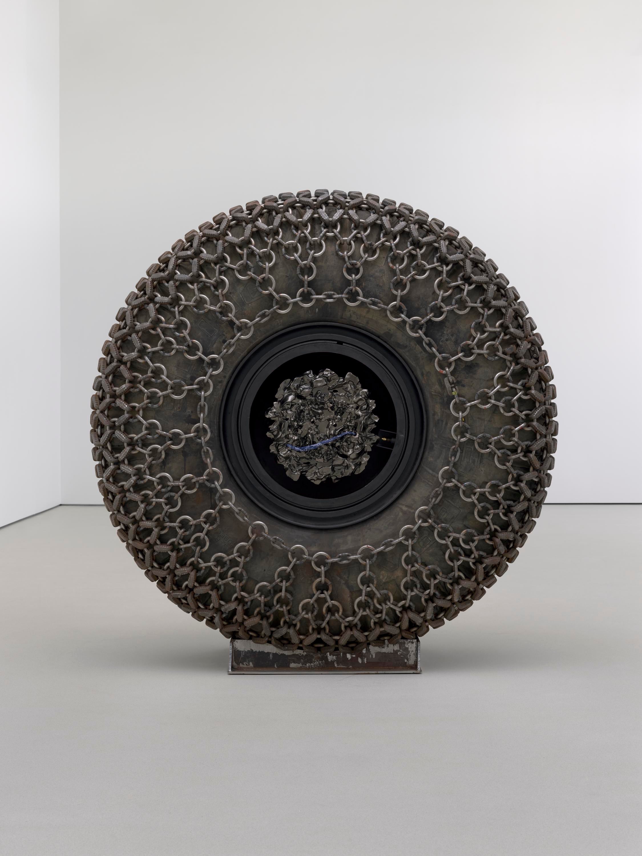 A large wheel wrapped in chains sits on a white floor.