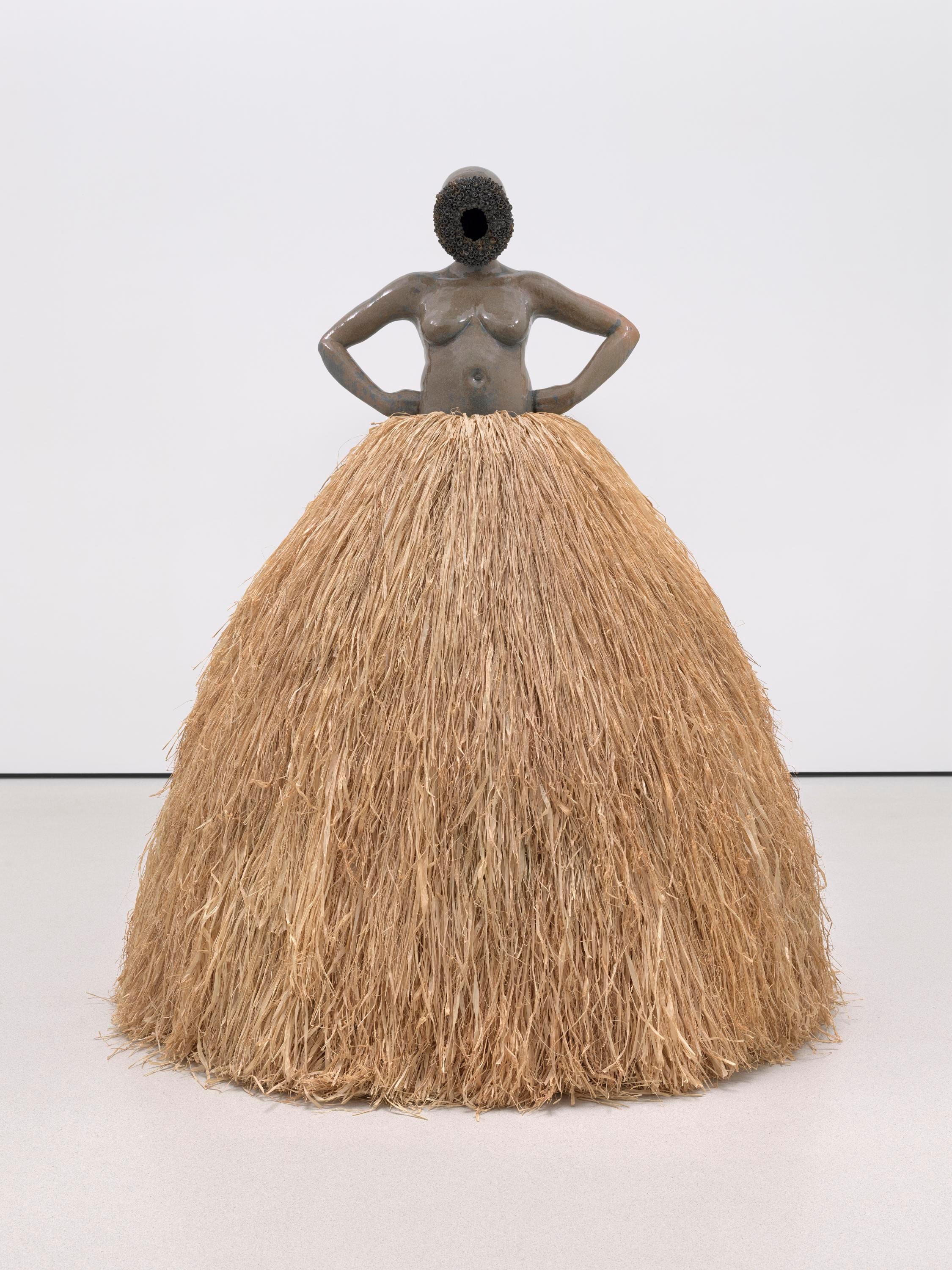 A statue of a woman with arms on her hips and a large raffia skirt stares at the viewer.