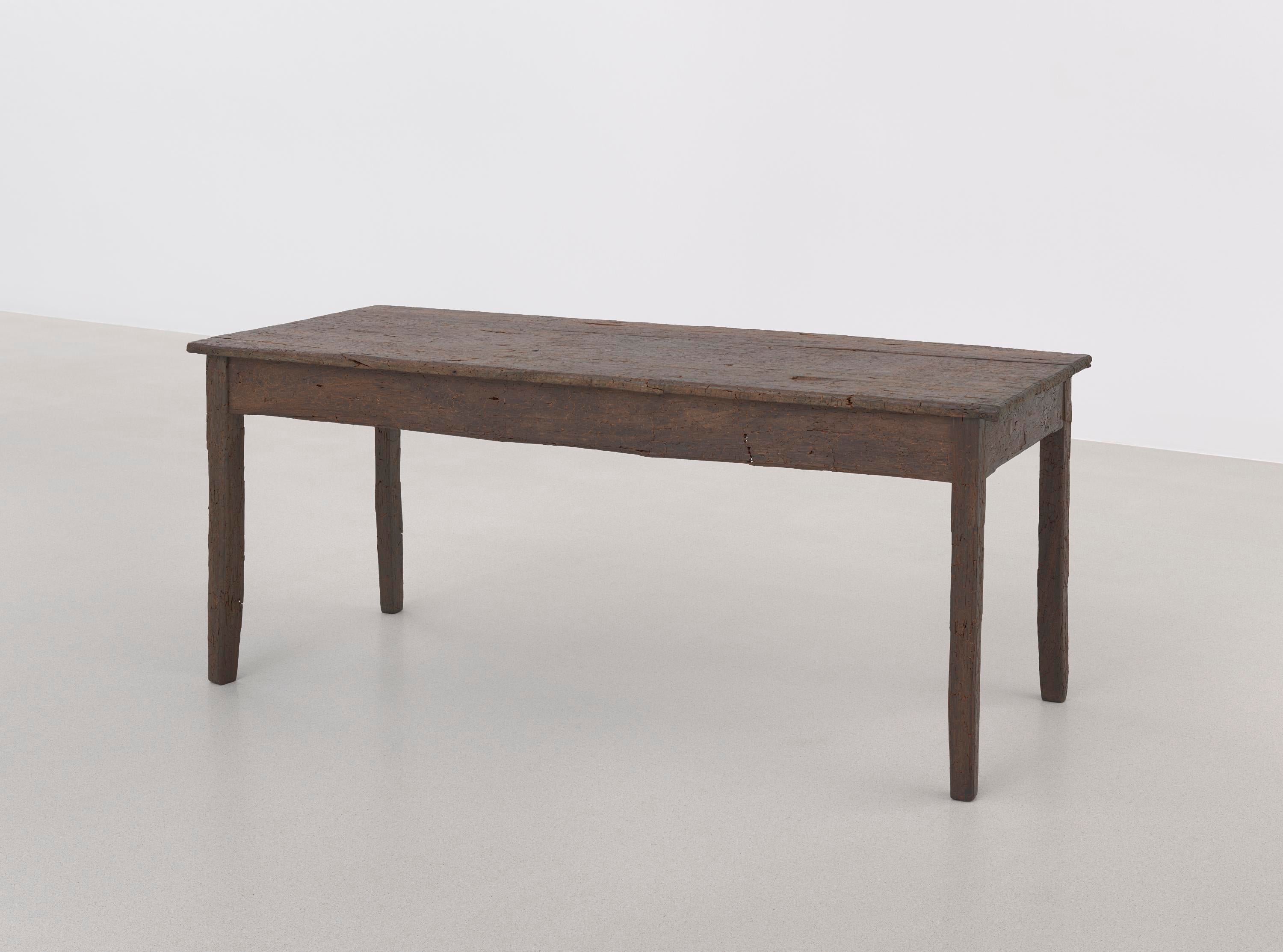 Una mesa de madera marrón se encuentra en el suelo de la galería y tiene una superficie rugosa e irregular.