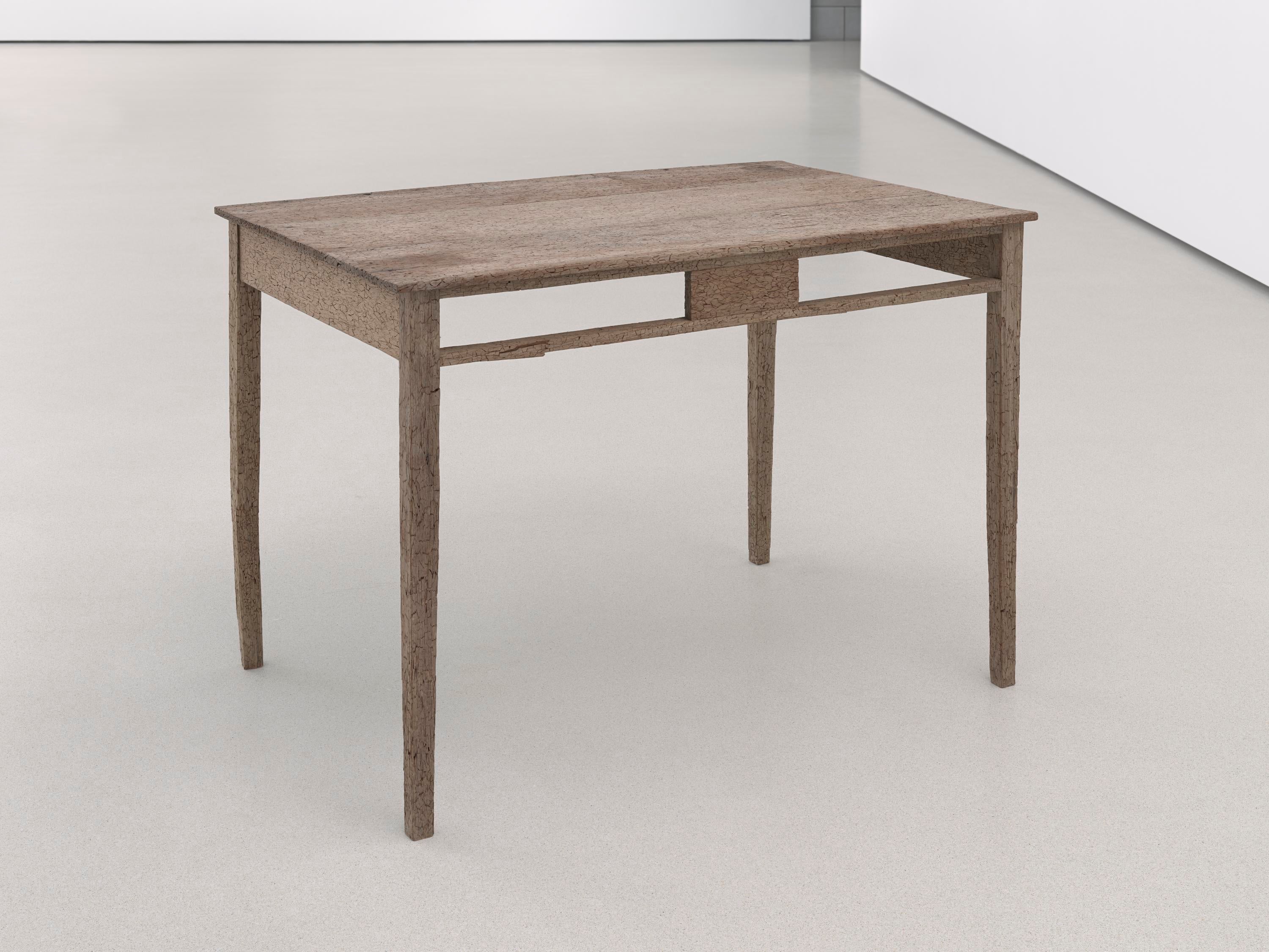 En el suelo hay un escritorio sin cajones con la superficie rugosa y dañada.