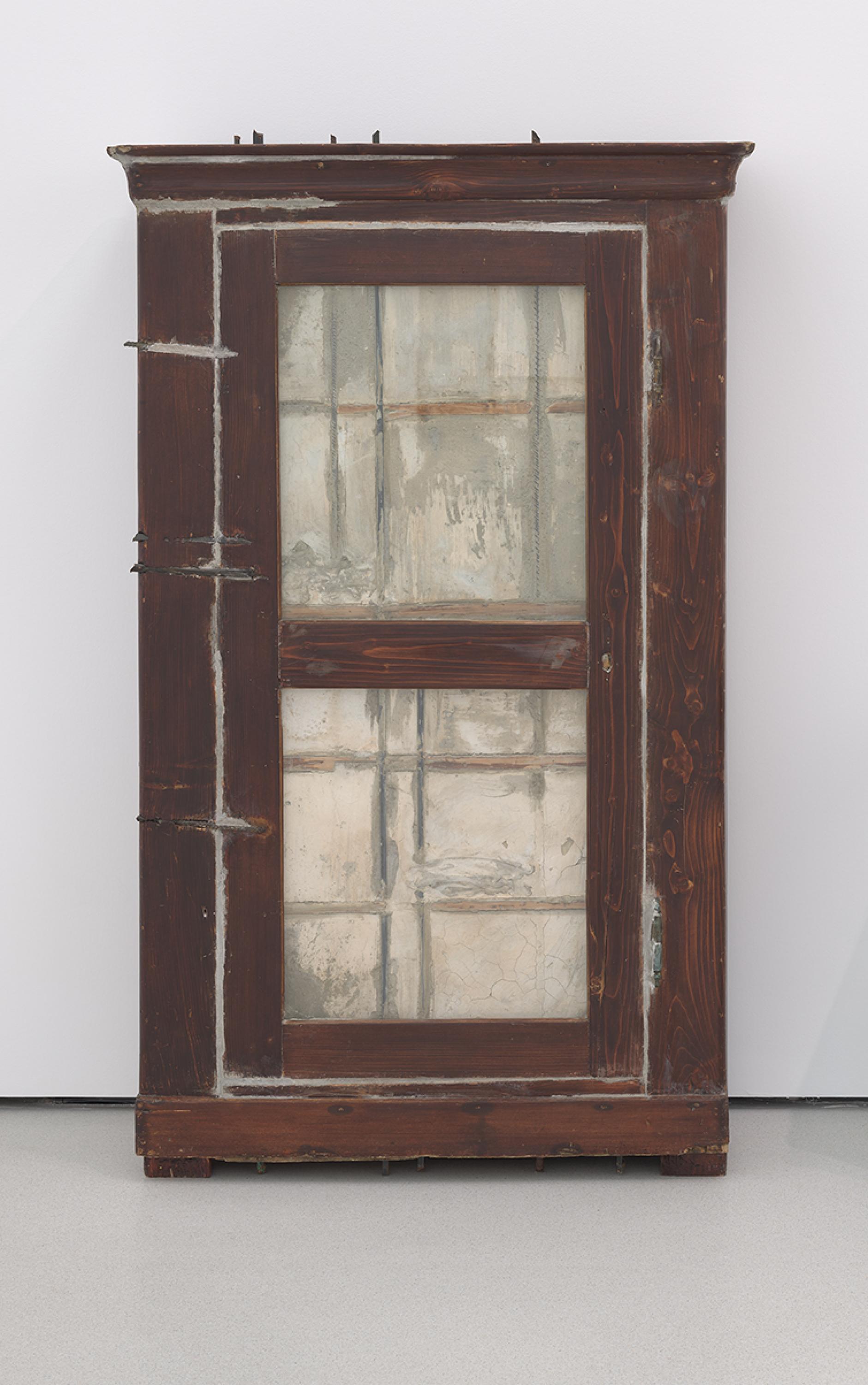 Un armario con frente de vidrio lleno de hormigón, apoyado contra una pared.