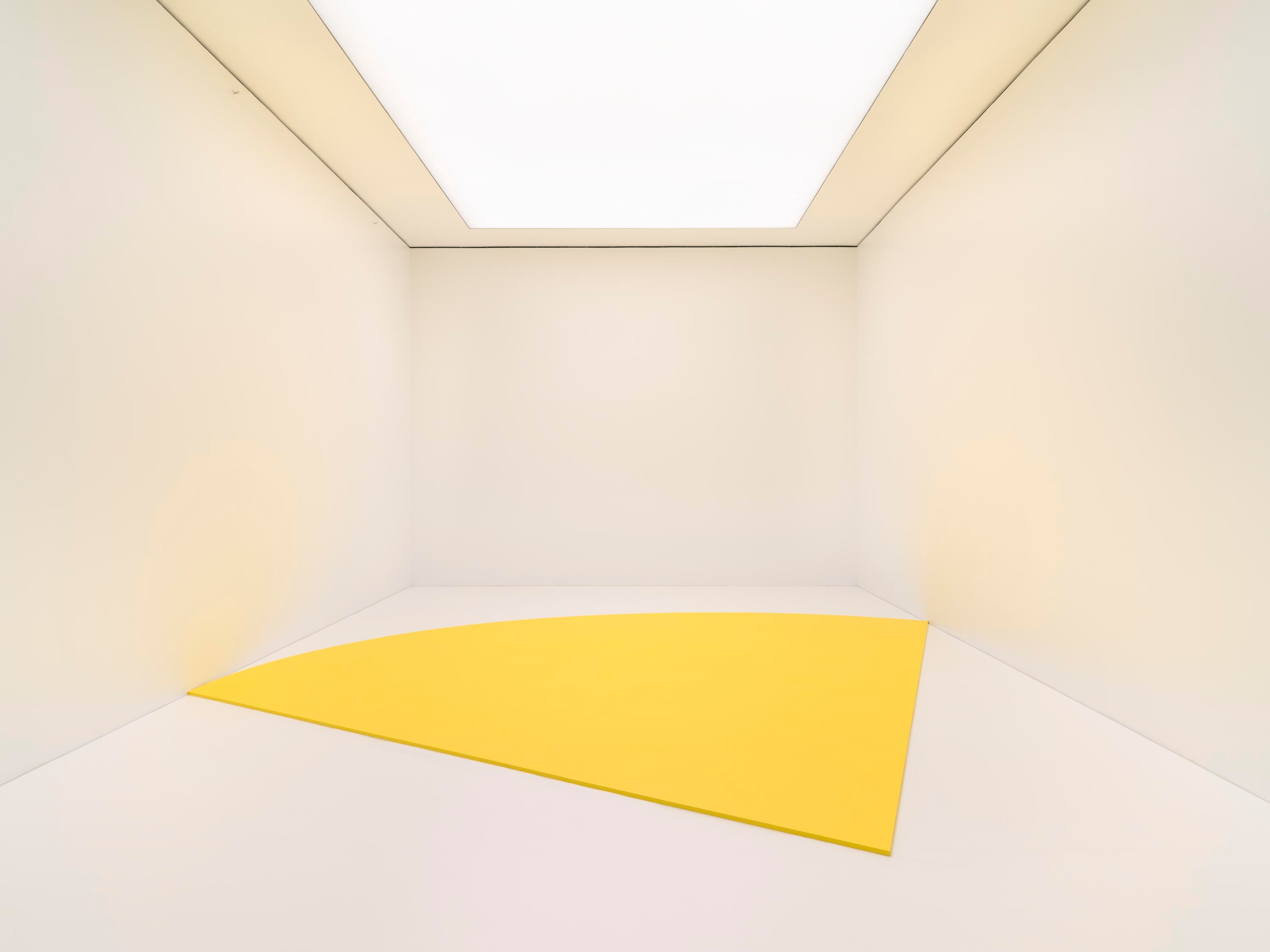 A large wedge of yellow sits on the floor of a white room, lit from above by a white lightwell.