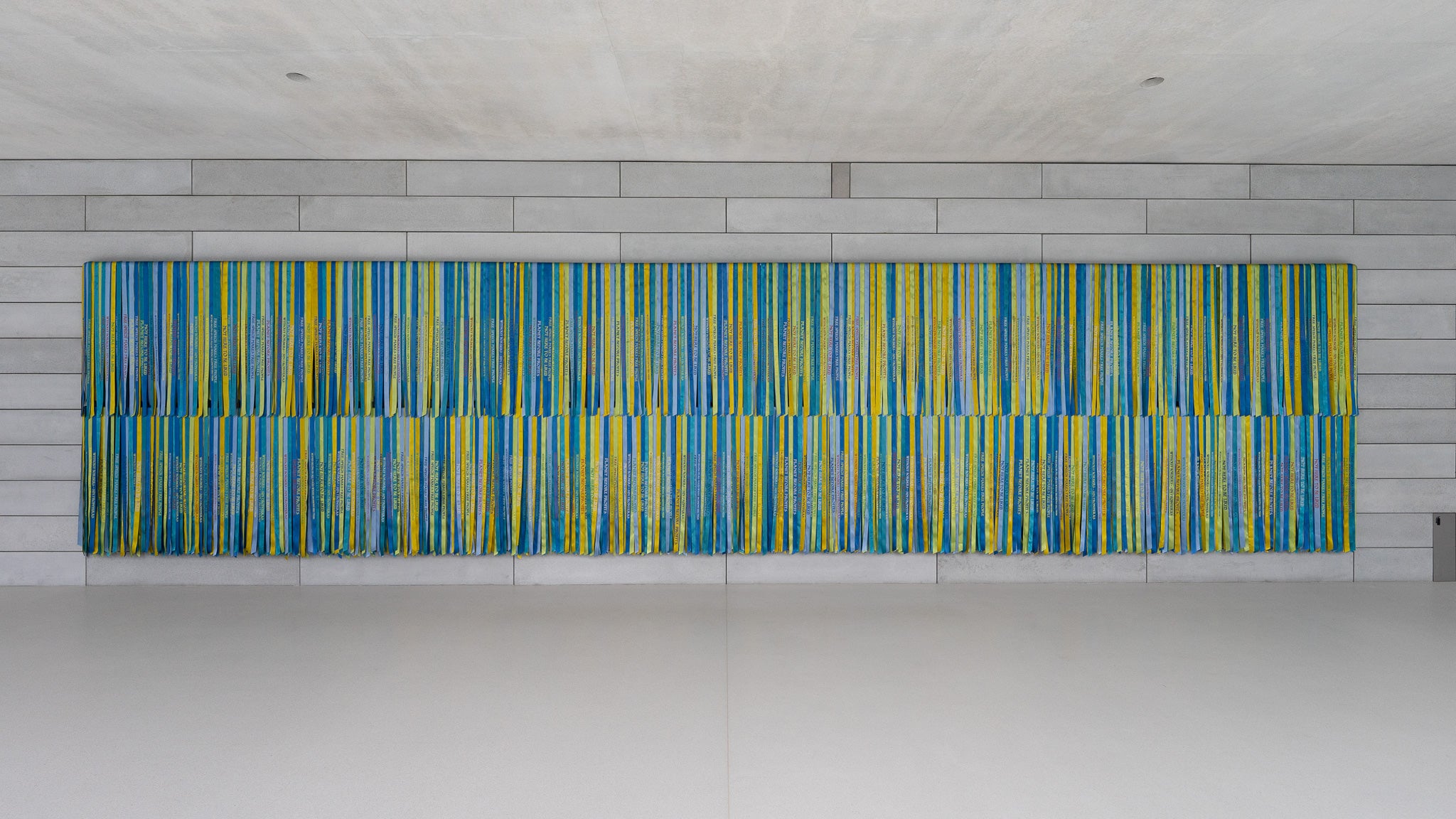 A selection of yellow, blue, and green ribbons hangs on a concrete wall