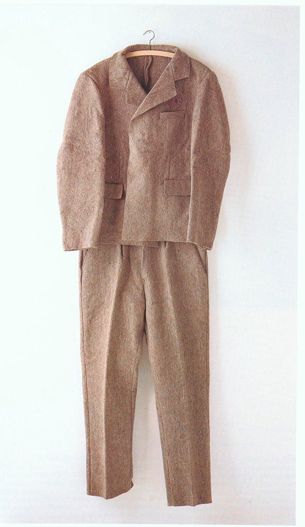 A tan suit on a clothes hanger hangs on a white wall.