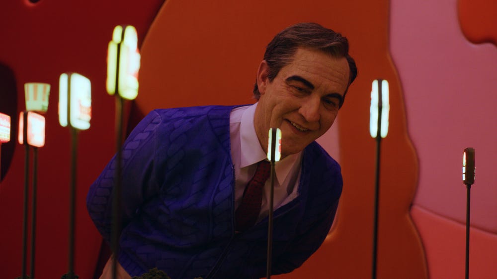 Alex Da Corte, dressed as Mister Rogers, looks at an artwork.