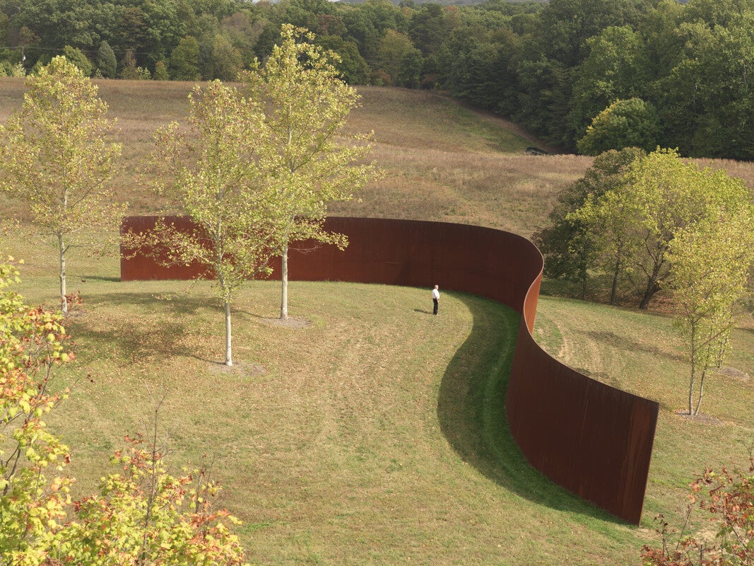 A large steel sculpture runs through a meadow