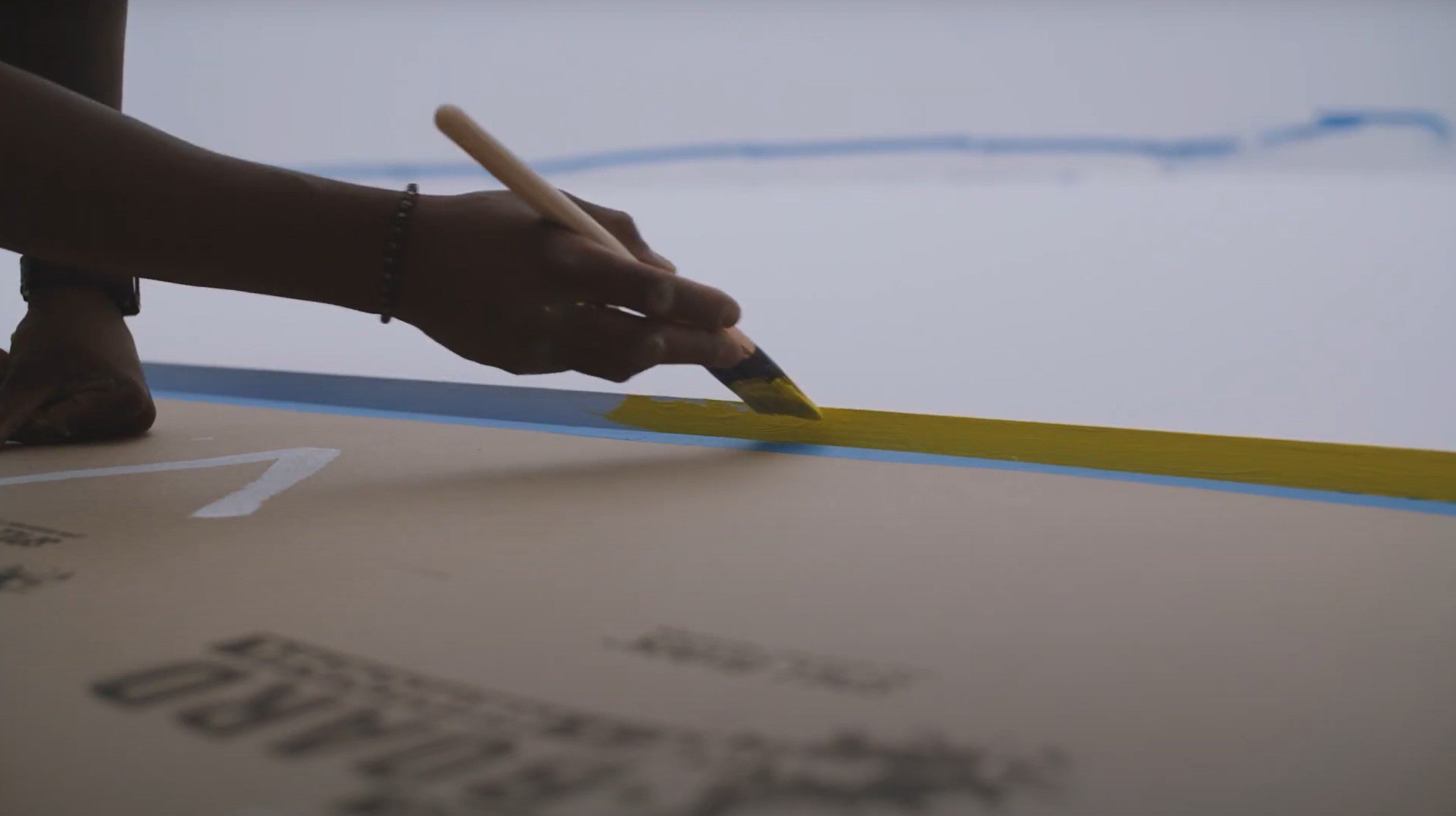A hand holds a brush covered in yellow paint.