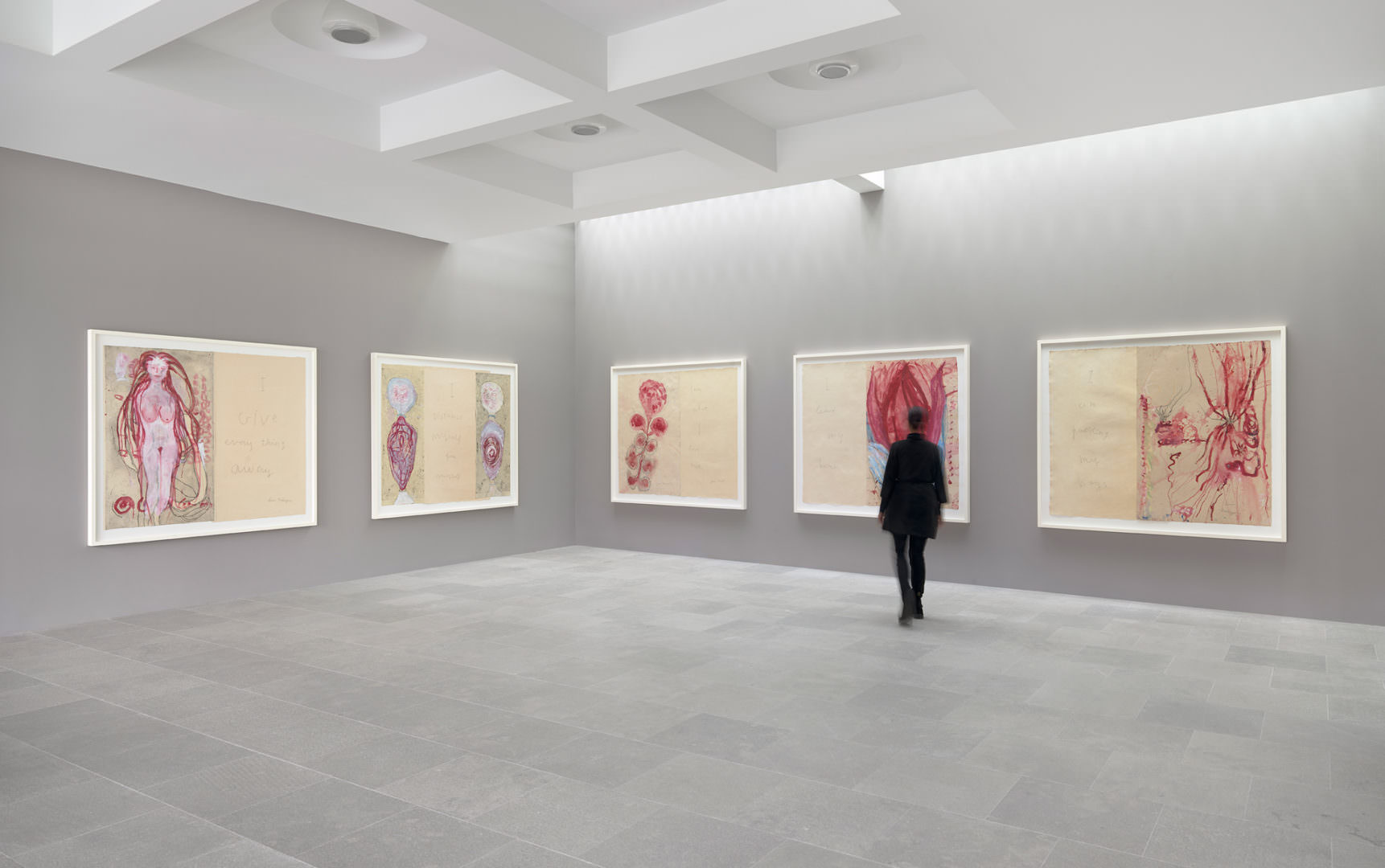 A blurred figure walks in a gray gallery space with a stone floor towards five large painted works on paper.