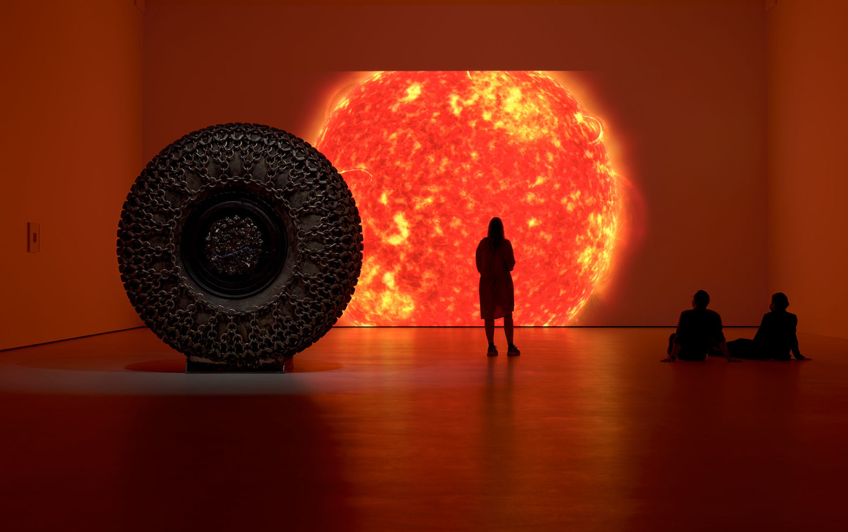 Several people stand and sit in a room in front of a large, projected sun.