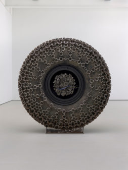 A large wheel wrapped in chains sits on a white floor.