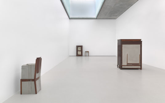 Four altered pieces of furniture sit in a white gallery space.