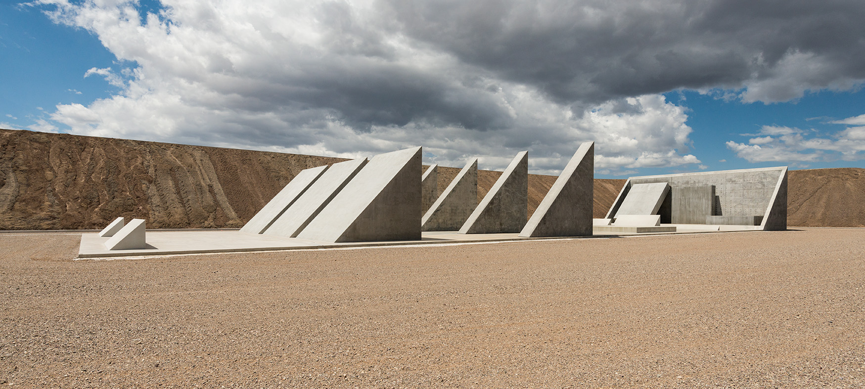 a series of triangular concrete forms sit on a flat plane in the desert